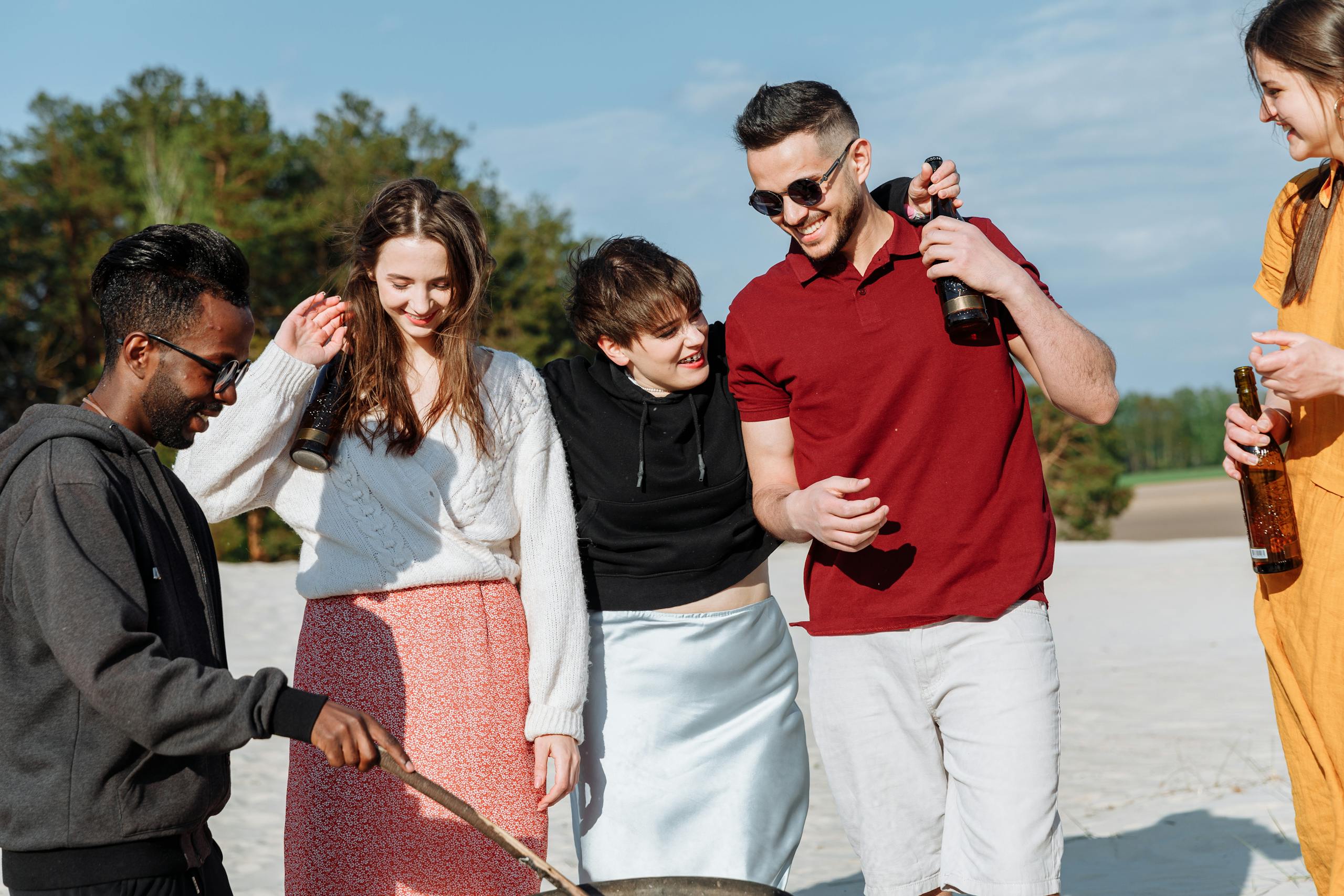 A group of diverse friends bonding on a sunny beach day with drinks and smiles.